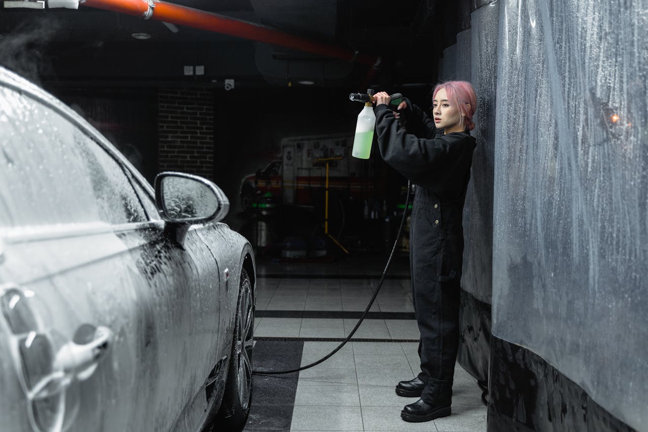services-02 A young woman uses a power spray to clean a car with foam in an indoor garage.